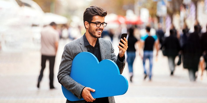 A smiling man with a mobile phone in one hand and a cut-out of a cloud in the other hand.